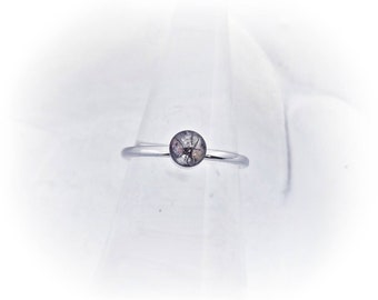 May include: A silver ring with a clear stone set in the center. The stone has a dark gray, spiderweb-like pattern.
