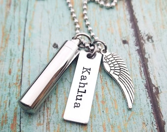 May include: Silver necklace with a small silver urn, a silver tag with the name "Kahlua" engraved on it, and a silver angel wing charm.