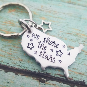 May include: Silver keychain featuring an outline of the United States with the text "we share the stars" and several small stars.