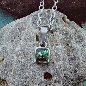 May include: A silver chain necklace with a square pendant featuring a green gemstone.