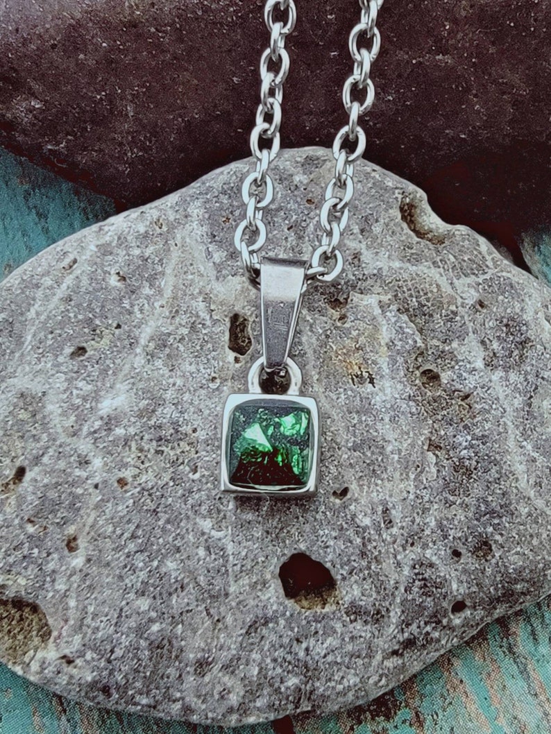 May include: A silver chain necklace with a square pendant featuring a green gemstone.