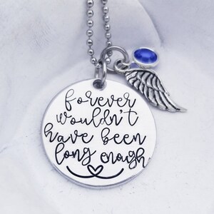 Puede incluir: Collar de plata con un colgante redondo que dice "forever wouldn't have been long enough" con un pequeño corazón en la parte inferior. El colgante está unido a una cadena de plata con una pequeña gema azul y un dije de ala de ángel de plata.