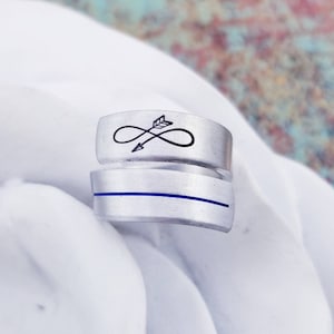 May include: A silver ring with a blue line and an infinity symbol with an arrow through it.