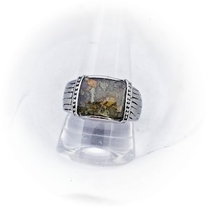 May include: A silver ring with a square-shaped green and brown stone set in the center. The ring has a textured band with a beaded edge.