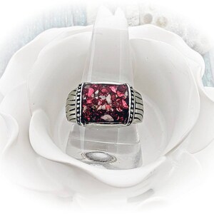 May include: A silver ring with a rectangular red and white stone inlay. The ring is set on a white background.