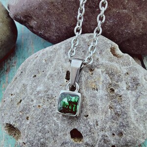 May include: A silver chain necklace with a square pendant featuring a dark green gemstone.