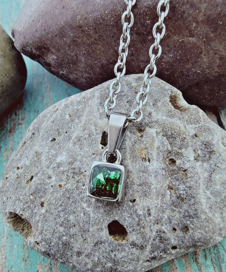 May include: A silver chain necklace with a square pendant featuring a dark green gemstone.
