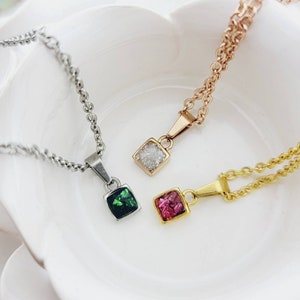 May include: Three silver chains with square pendants. The pendants are filled with crushed glass in green, pink, and white.