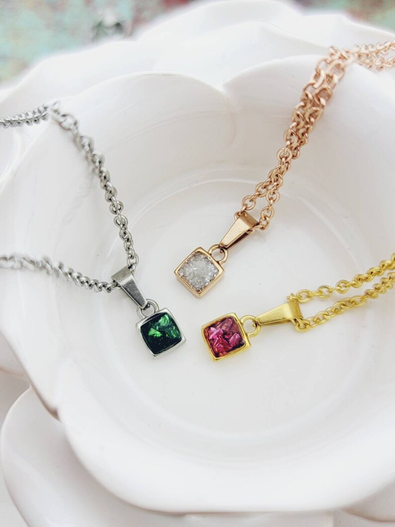 May include: Three silver chains with square pendants. The pendants are filled with crushed glass in green, pink, and white.