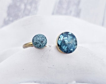 May include: Two gold rings with blue stone settings. One ring has a round, textured blue stone. The other ring has a round, sparkly blue stone.