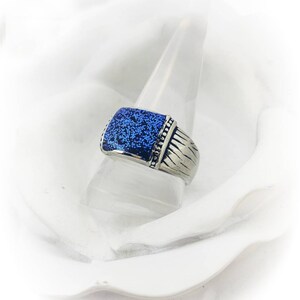 May include: A silver ring with a blue square stone set in the center. The stone has a textured surface.