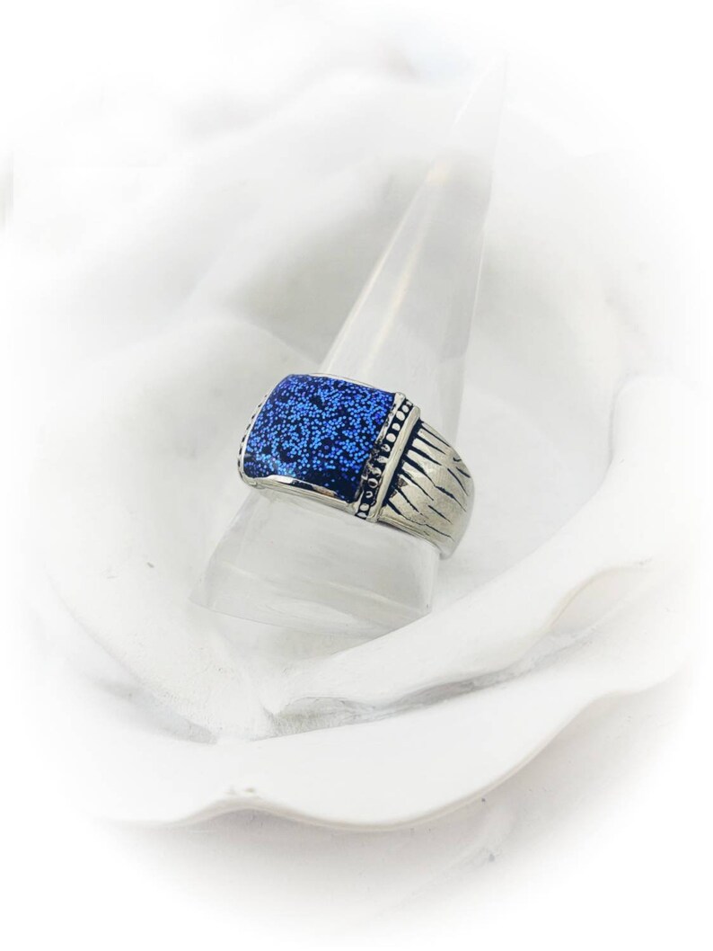 May include: A silver ring with a blue square stone set in the center. The stone has a textured surface.
