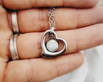 May include: A silver heart-shaped pendant necklace with a small, round, white opal-like stone in the center.