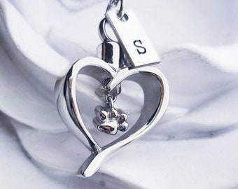 May include: Silver heart-shaped cremation necklace with a paw print charm and a tag engraved with the letter "S".