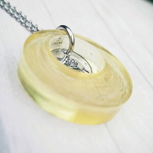 May include: A pendant necklace with a clear, oval resin, displaying a yellow and white swirl pattern. Inside the resin is a small, silver charm with a paw print. The necklace has a silver chain.