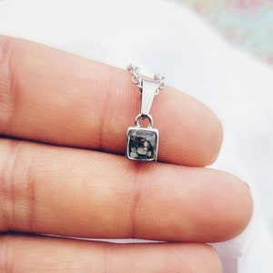 May include: A silver chain necklace with a square pendant featuring a dark gray and white stone.