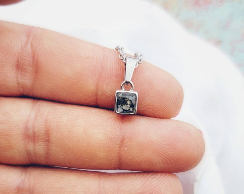 May include: A silver chain necklace with a square pendant featuring a dark gray and white stone.