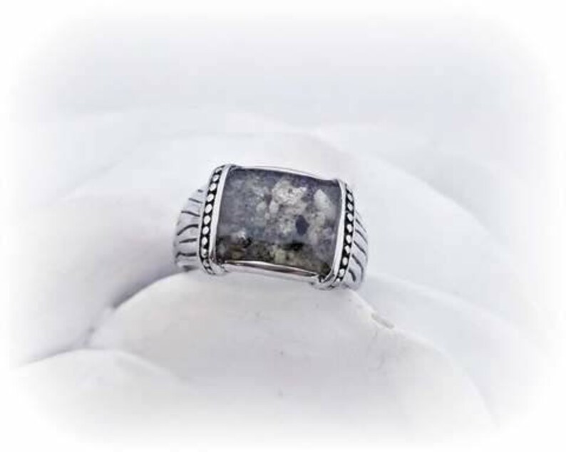 May include: A silver ring with a rectangular gray stone set in the center. The stone has a speckled pattern and is surrounded by a beaded border.