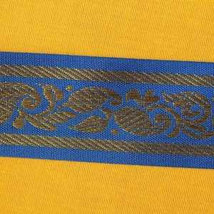 Puede incluir: Primer plano de una tela amarilla con un ribete azul y dorado. El ribete presenta un patrón repetido de diseños florales estilizados.