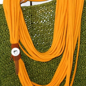 May include: A bright orange infinity scarf made of soft fabric with a silver heart charm on a brown leather strap.