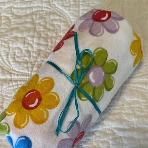 May include: A white fabric blanket with a colorful floral pattern. The blanket is rolled up and tied with a turquoise ribbon.