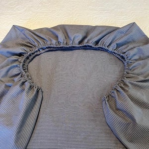 May include: A gray and white striped fitted sheet with elastic all around the edges.