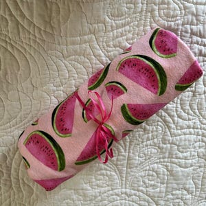 May include: A pink fabric with a watermelon print. The fabric is rolled up and tied with a pink ribbon.