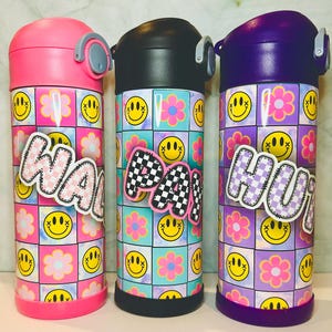 Puede incluir: Tres botellas de agua de acero inoxidable con tapas de colores y un patrón de tie-dye. Las botellas tienen una pegatina a cuadros con las palabras "Wavy", "Party" y "Hunky" en ellas.