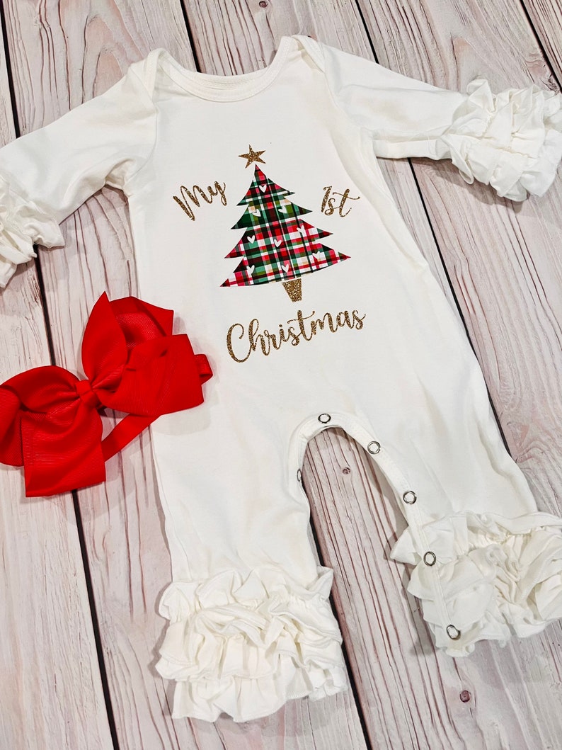 May include: White baby onesie with a gold glitter design of a Christmas tree with red and green plaid and the text "My 1st Christmas".