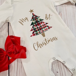 May include: White baby onesie with a gold glitter design of a Christmas tree with red and green plaid and the text "My 1st Christmas".