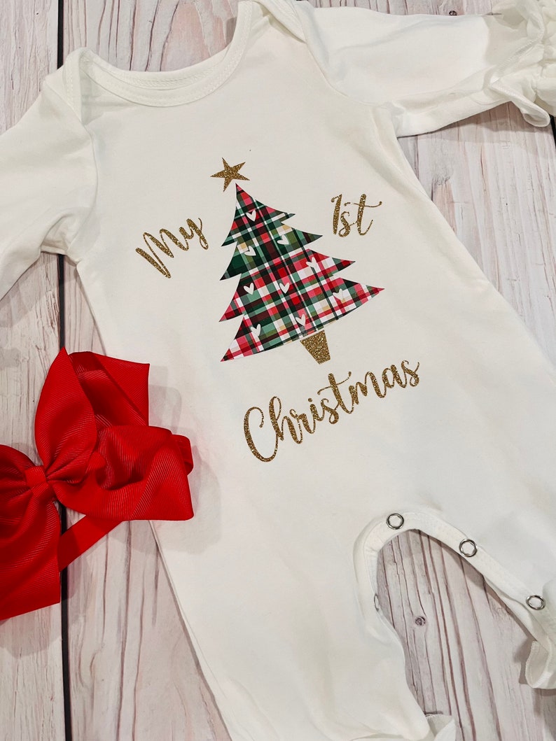 May include: White baby onesie with a gold glitter design of a Christmas tree with red and green plaid and the text "My 1st Christmas".