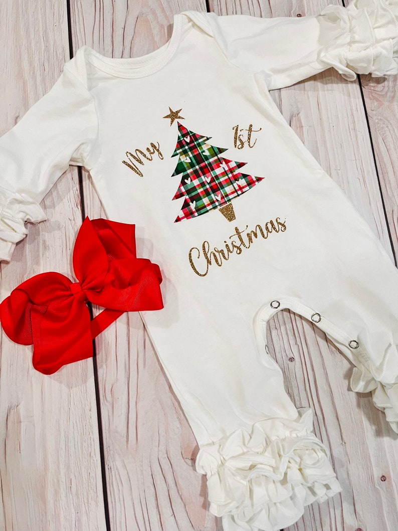 May include: White baby onesie with a green, red, and white plaid Christmas tree with gold glitter and the text "My 1st Christmas". A red bow is included.