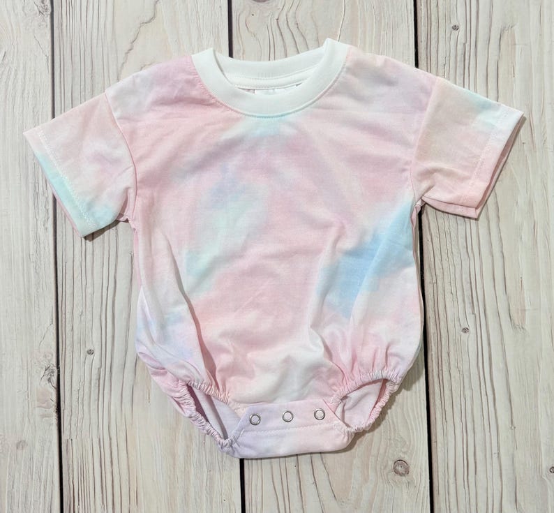 Może przedstawiać: Body niemowlęce z kr&oacute;tkim rękawem z wzorem tie-dye w delikatnych pastelowych odcieniach r&oacute;żu, błękitu i bieli. Ubranko posiada jednolity biały okrągły dekolt oraz trzy metalowe zatrzaski w kroku, kt&oacute;re zapewniają bezpieczne i łatwe zapięcie.