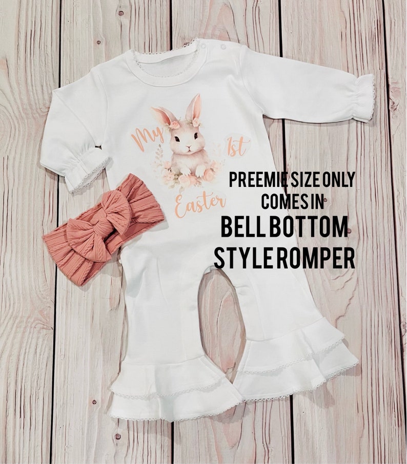 K&ouml;nnte beinhalten: Wei&szlig;er Baby Strampler mit einem Hasen- und Blumendesign. Der Strampler sagt "Mein 1. Ostern". Er kommt im Glockenbein-Stil. Ein pfirsichfarbenes Stirnband ist enthalten.