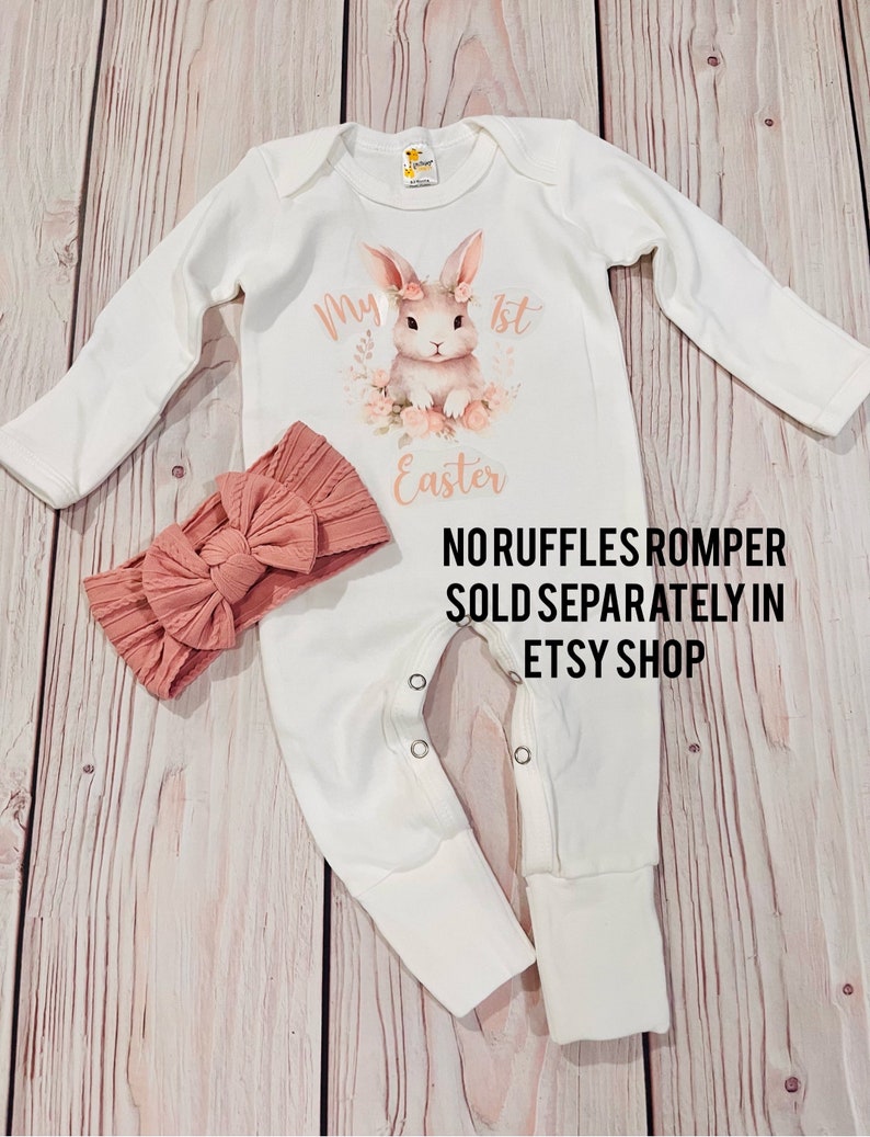 K&ouml;nnte beinhalten: Wei&szlig;er lang&auml;rmliger Baby-Strampler mit einem rosa Hasen-Motiv und dem Text "My 1st Easter". Ein rosa Schleifen-Stirnband ist ebenfalls enthalten. Der Text "Noruffles Romper Sold Separately in Etsy Shop" ist unter dem Motiv gedruckt.