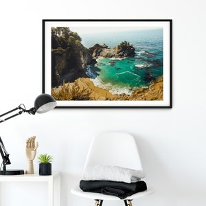 May include: A framed photograph of a scenic coastal landscape. The image shows a rocky cove with a small beach and turquoise water. Lush green trees and cliffs surround the cove. The water is clear and calm, with a few small waves breaking on the shore.