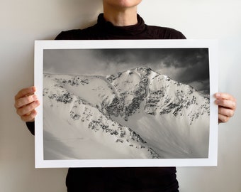 Puede incluir: Una fotografía en blanco y negro de una cordillera cubierta de nieve. Los picos de las montañas son afilados y dentados, y las laderas están cubiertas de una gruesa capa de nieve. El cielo está nublado y la luz es suave y difusa.
