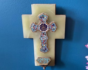 May include: A decorative wall cross with a light green onyx base. The cross features an ornate, colorful design with blue, red, and gold accents. A small, matching container is below the cross.