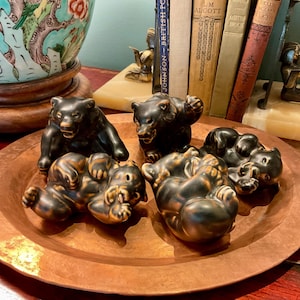 Pode incluir: Uma coleção de cinco pequenas figuras de urso em cerâmica castanho-escura dispostas numa bandeja grande, redonda e de cobre martelado. Os ursos são representados em várias poses, incluindo de pé, sentados e deitados, com superfícies lisas e brilhantes.