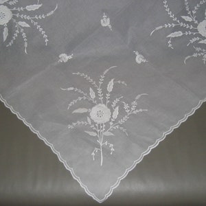 May include: White embroidered tablecloth with a scalloped edge and floral designs.