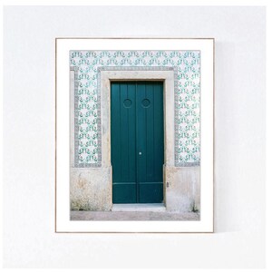 May include: A teal green door with two panels and a circular handle. The door is framed by a white stone archway and surrounded by white and green patterned tiles.