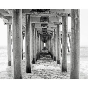 Pode incluir: Uma fotografia a preto e branco de um cais que se estende sobre o oceano. O cais &eacute; feito de bet&atilde;o e tem muitos pilares. A &aacute;gua est&aacute; agitada e h&aacute; uma pequena abertura no final do cais.