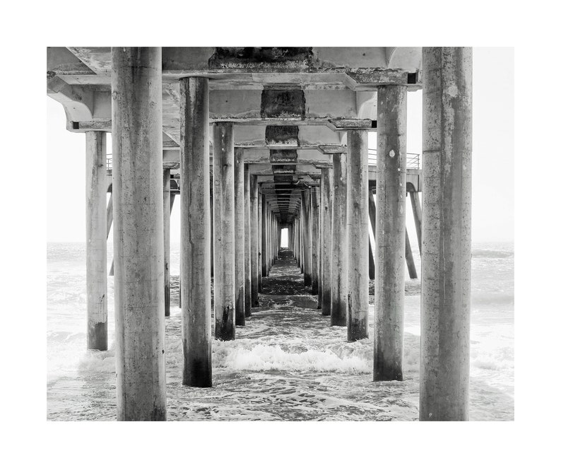 Pode incluir: Uma fotografia a preto e branco de um cais que se estende sobre o oceano. O cais &eacute; feito de bet&atilde;o e tem muitos pilares. A &aacute;gua est&aacute; agitada e h&aacute; uma pequena abertura no final do cais.