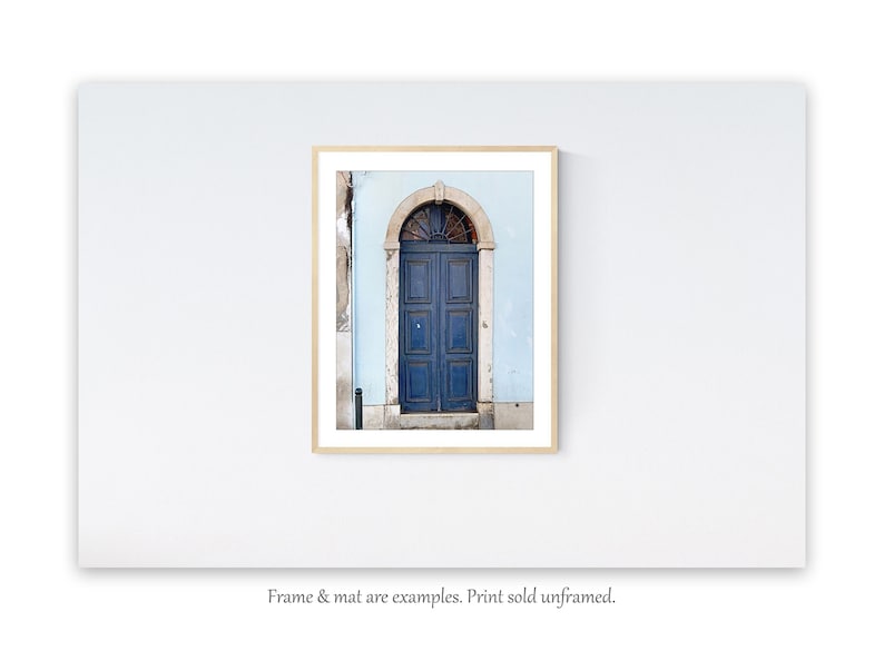 May include: A photograph of a blue door with a decorative arched window above it. The door is set in a light blue wall. The door is made of wood and has a simple design. The door is closed and there is a small step leading up to it.