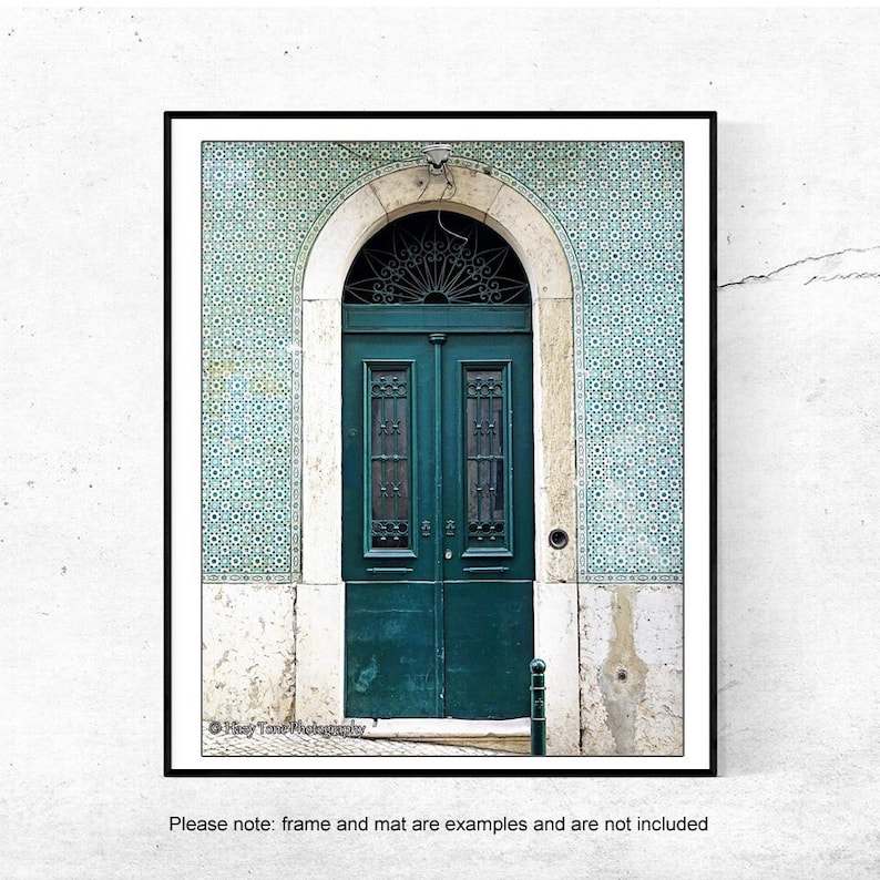 May include: A green wooden door with a decorative iron grate and a small window above the door. The door is set in a white stone archway with blue and white patterned tiles on either side.