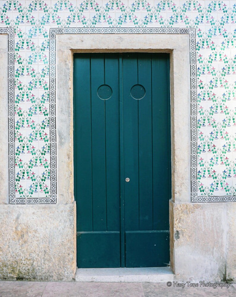 May include: A teal green double door with a white trim and a white and green tiled wall behind it.