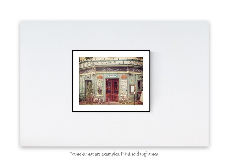 May include: A vintage photograph of a Parisian restaurant called "Le Petit Zinc". The building is painted a pale blue-green with a red door and a sign above the entrance. There are tables and chairs set up outside the restaurant.