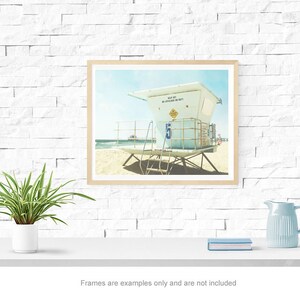 May include: A framed photograph of a lifeguard stand on a beach. The stand is white with a blue sign that reads "Keep Out Of Water When Red Flags Are Displayed".