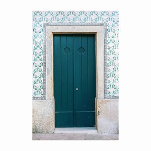 May include: A teal green double door with two circular door knockers, set in a stone doorway with a white and green tiled wall.