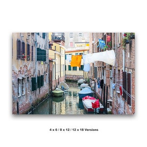 May include: A narrow canal in Venice, Italy, with colorful buildings lining the sides.  Laundry hangs on lines strung across the canal.  Several small boats are moored in the water.